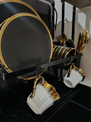 Un escurreplatos negro y dorado con platos, tazones y tazas.