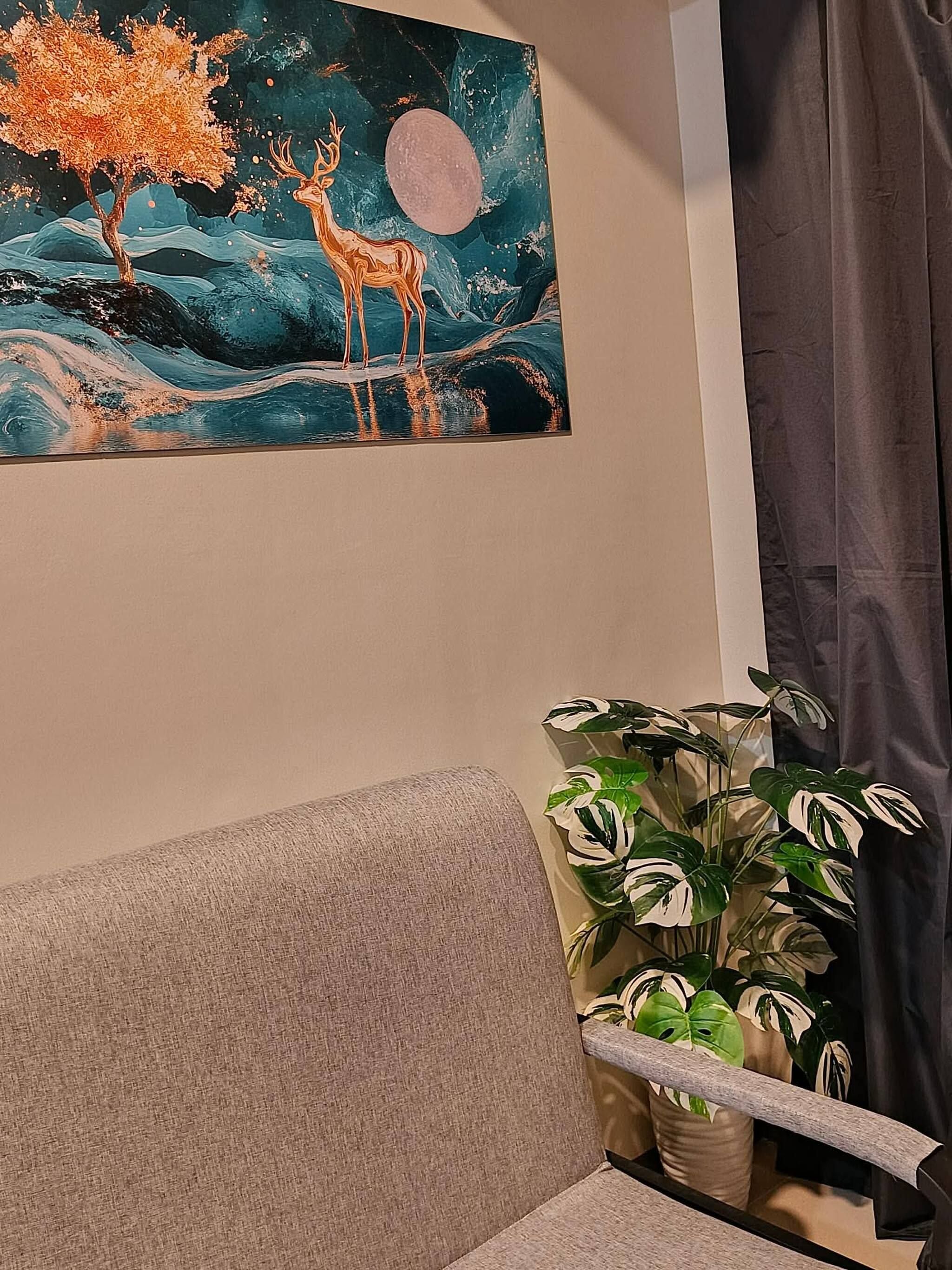 Una habitación con un sofá, un cuadro de un ciervo y un árbol, y una planta en maceta.