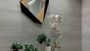 Un interior moderno con un espejo geométrico, una escultura metálica y plantas en macetas sobre una consola.
