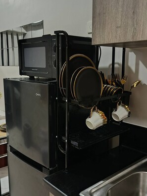 A kitchen with a black refrigerator, a microwave, and a dish rack holding plates, cups, and utensils. - Modern, Comfortable Apartment in Central Pasay, Philippines (Pasay)