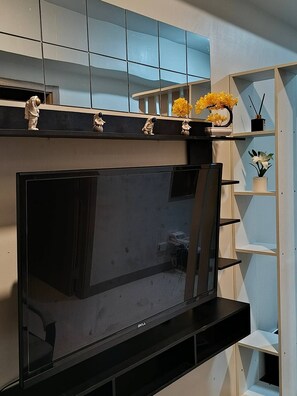 A flat-screen TV mounted on a wall with a shelf above it holding decorative items. - Modern, Comfortable Apartment in Central Pasay, Philippines (Pasay)
