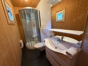 Ein kleines Badezimmer mit einer Duschkabine, einer Toilette und einem Waschbecken mit Spiegel darüber.