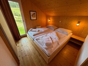 A wooden cabin bedroom with a bed, a window, and a wall-mounted light. - Chalet Murau West 21a (Murau)