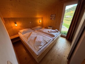 A wooden room with a bed, two wall-mounted lights, and a window with a view of greenery. - Chalet Murau West 21a (Murau)