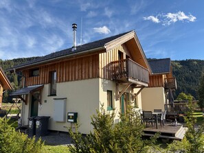 A two-story wooden building with a balcony, outdoor seating, and a view of a forested mountain. - Chalet Murau West 21b (Murau)