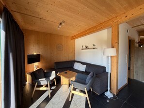 Ein gemütliches Wohnzimmer mit einer Couch, Sesseln, einem Couchtisch und einem Fernseher.