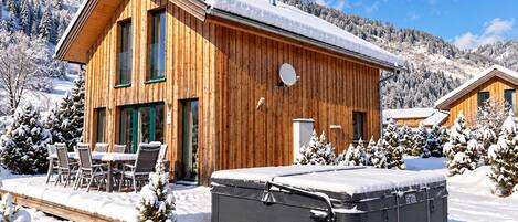 En træhytte med jacuzzi og terrasse, omgivet af sneklædte træer og et bjerglandskab.