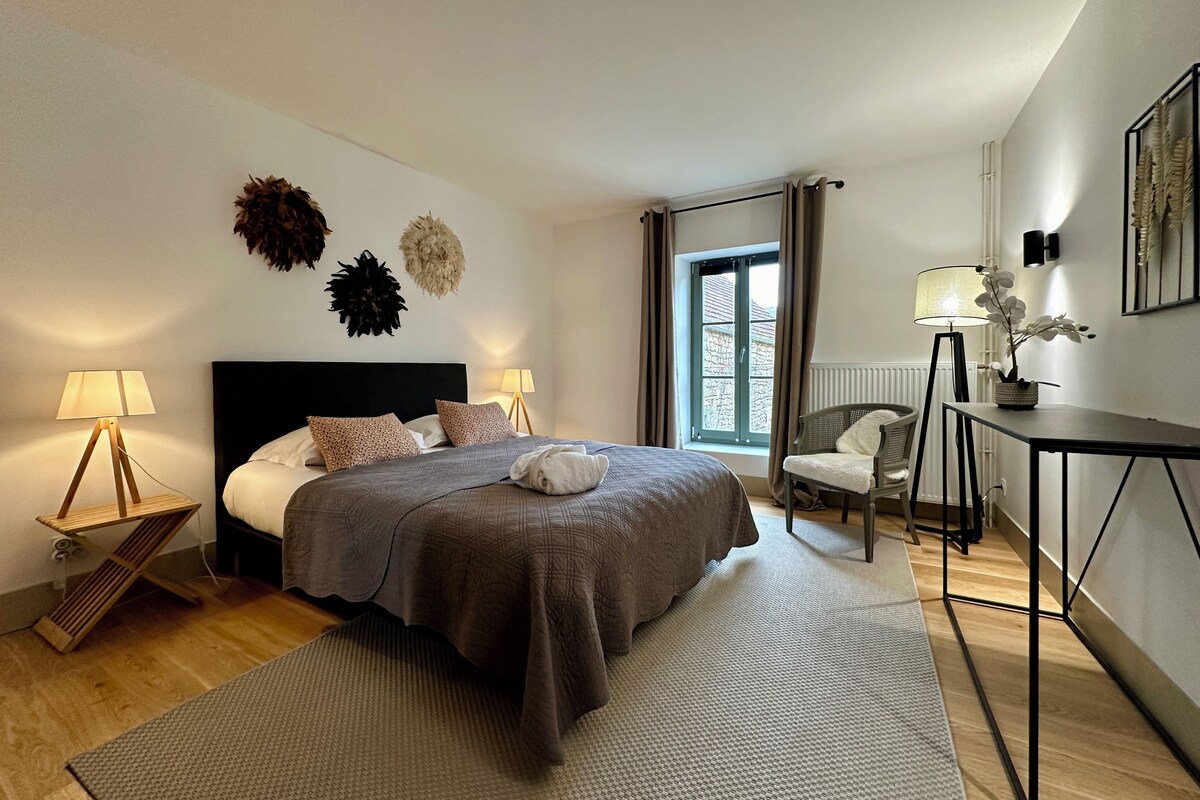 Ein modernes Schlafzimmer mit einem großen Bett, zwei Nachttischlampen, einem Sessel, einem Schreibtisch und einem Fenster mit Vorhängen.