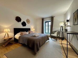 A modern bedroom with a large bed, two bedside lamps, a chair, a desk, and a window with curtains. - Maison Marguerite (Gigny)