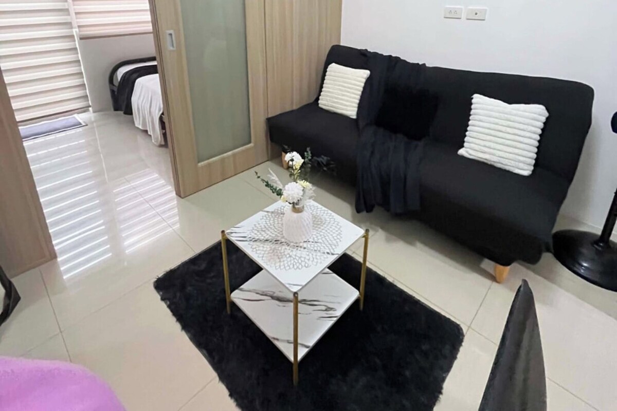 Een moderne woonkamer met een zwarte bank, een glazen salontafel en een deur die naar een andere kamer leidt.