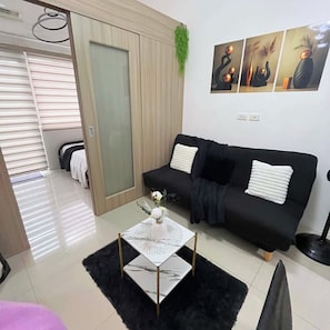 Una sala moderna con un sofá negro, una mesa de centro de vidrio y una puerta que da a otra habitación.