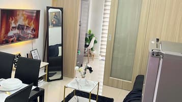 Un salon moderne doté d’un téléviseur à écran plat, d’un coin repas avec une table et des chaises, d’un grand miroir et d’une porte coulissante donnant sur une autre pièce.