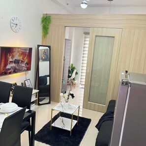 Una sala moderna con televisor de pantalla plana, comedor con mesa y sillas, un espejo grande y una puerta corredera que da a otra habitación.