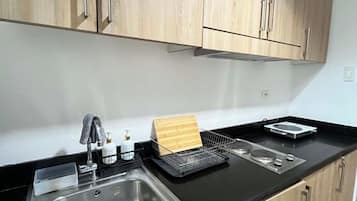 A kitchen with a stainless steel sink, wooden cabinets, a black countertop, and various kitchen items.