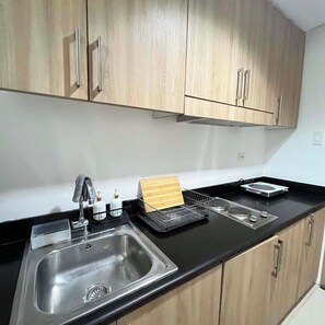 A kitchen with a stainless steel sink, wooden cabinets, a black countertop, and various kitchen items. - Staycation Suites PH (Pasay City)