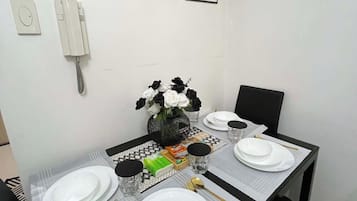 A dining table set with white plates, gold cutlery, and black and white flowers in a vase.