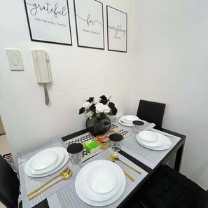 A dining table set with white plates, gold cutlery, and black and white flowers in a vase. - Staycation Suites PH (Pasay City)