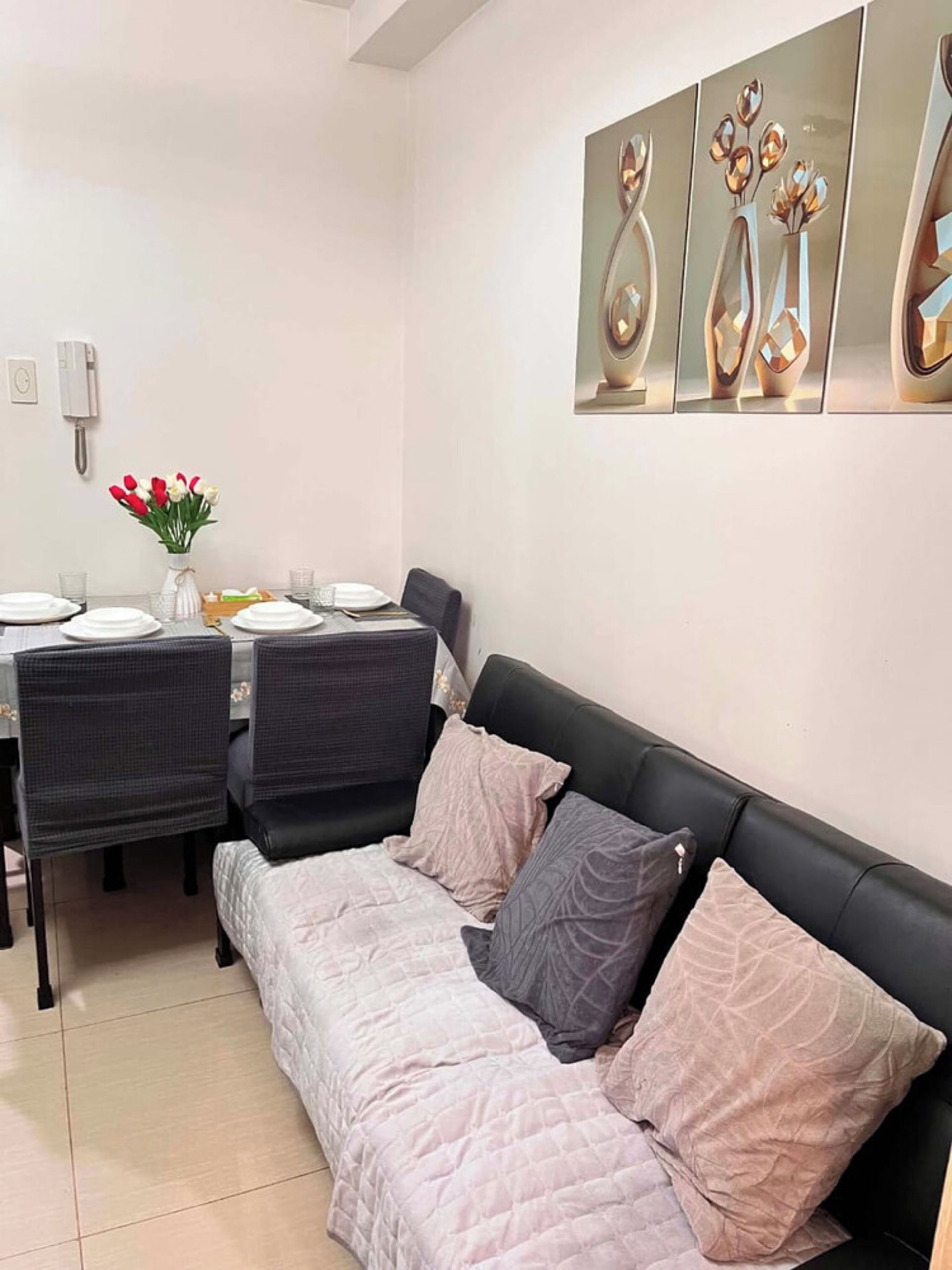 Un coin repas avec une table dressée pour quatre personnes, un canapé en cuir noir et une œuvre d’art abstraite accrochée au mur.