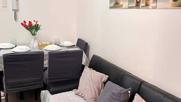 Un coin repas avec une table dressée pour quatre personnes, un canapé en cuir noir et une œuvre d’art abstraite accrochée au mur.