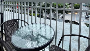 Un balcon avec une table et des chaises en verre, donnant sur une rue de la ville, avec des immeubles et une grue de construction.