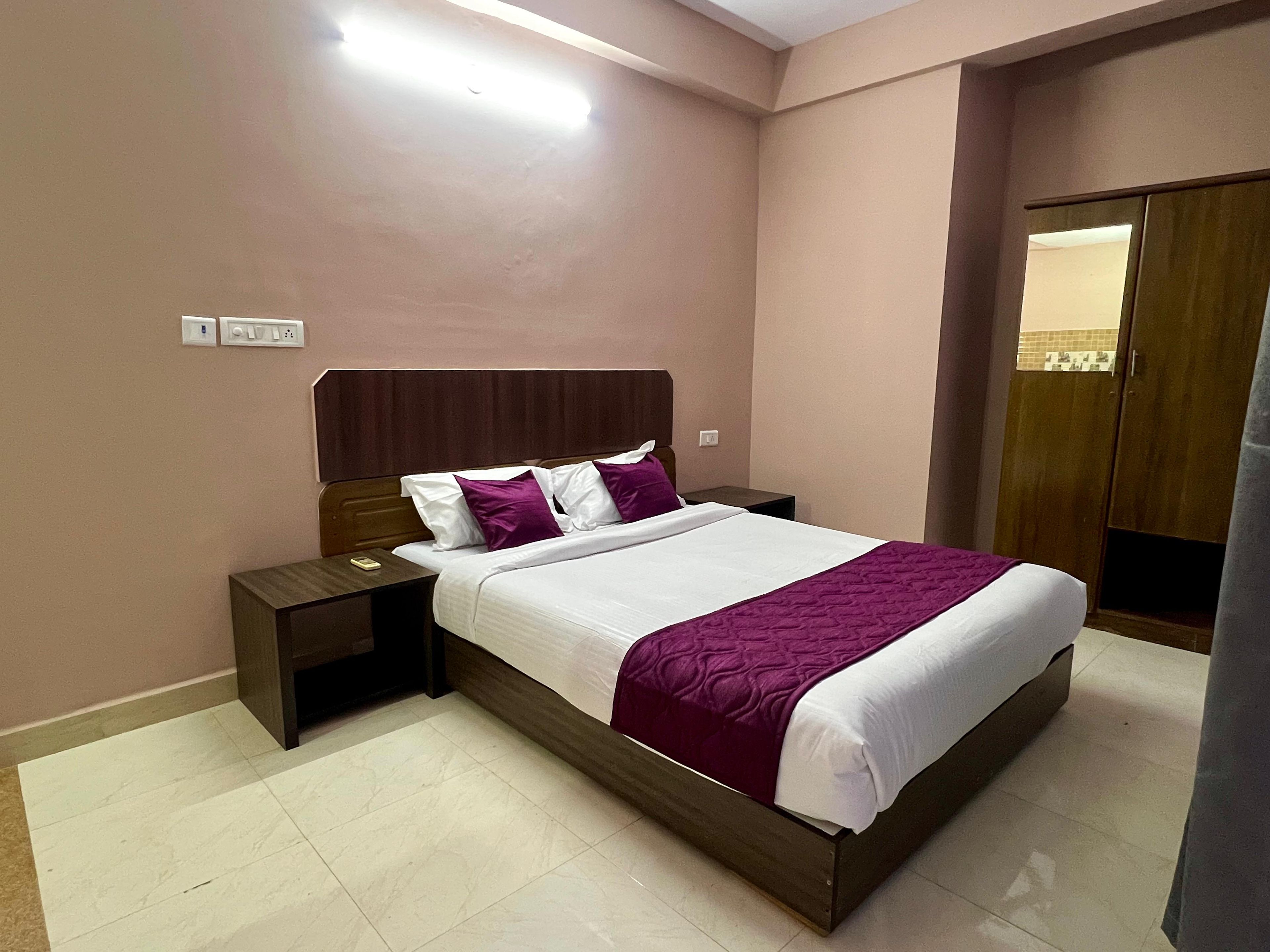 Una habitación de hotel con una cama, mesitas de noche, un cabecero de madera y un armario.