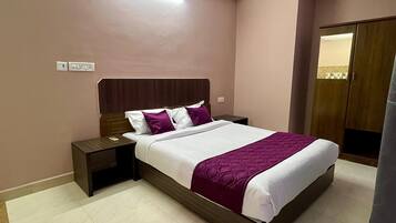 Una habitación de hotel con una cama, mesitas de noche, un cabecero de madera y un armario.