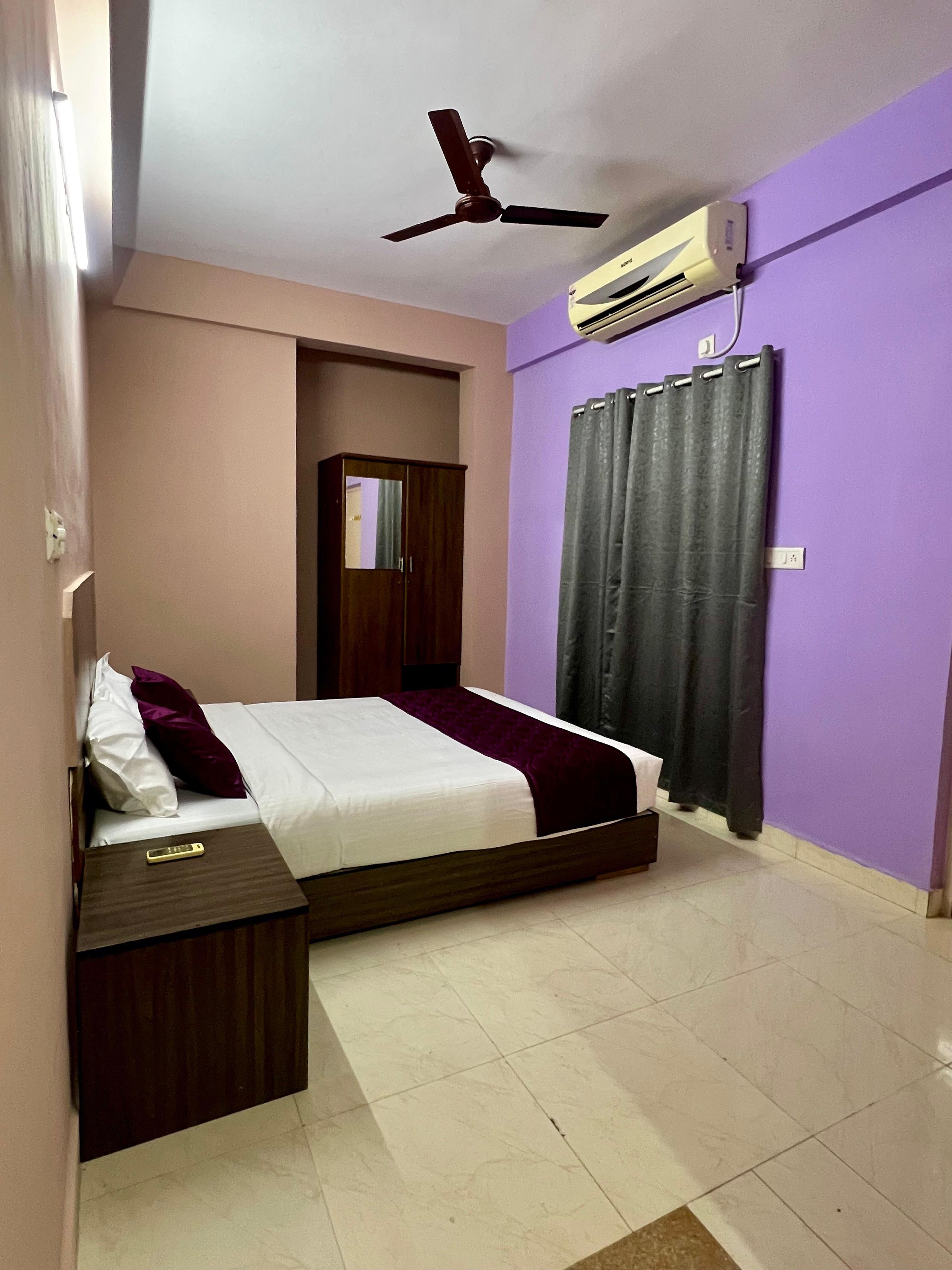 A bedroom with a bed, a ceiling fan, an air conditioning unit, a wardrobe, and a curtain.