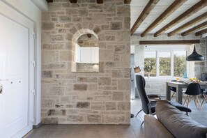 A stone-walled room with a wooden ceiling, a dining area with a table and chairs, and a view of the outdoors. - Villa Elies be a part of Crete (Mesi)