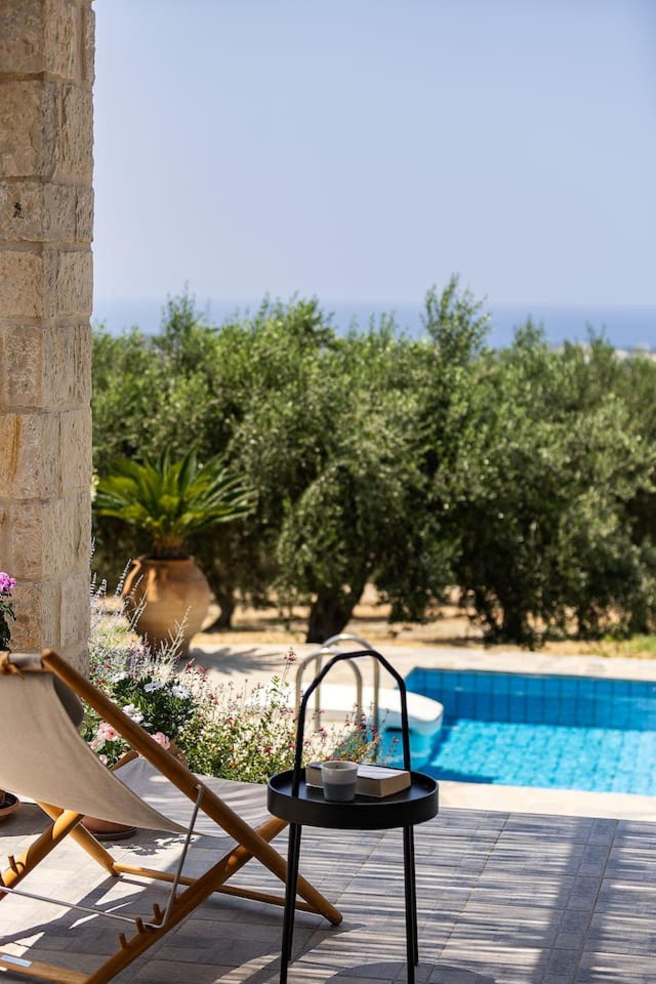 A poolside area with a lounge chair, a small table with a tray, and a view of the sea and greenery.