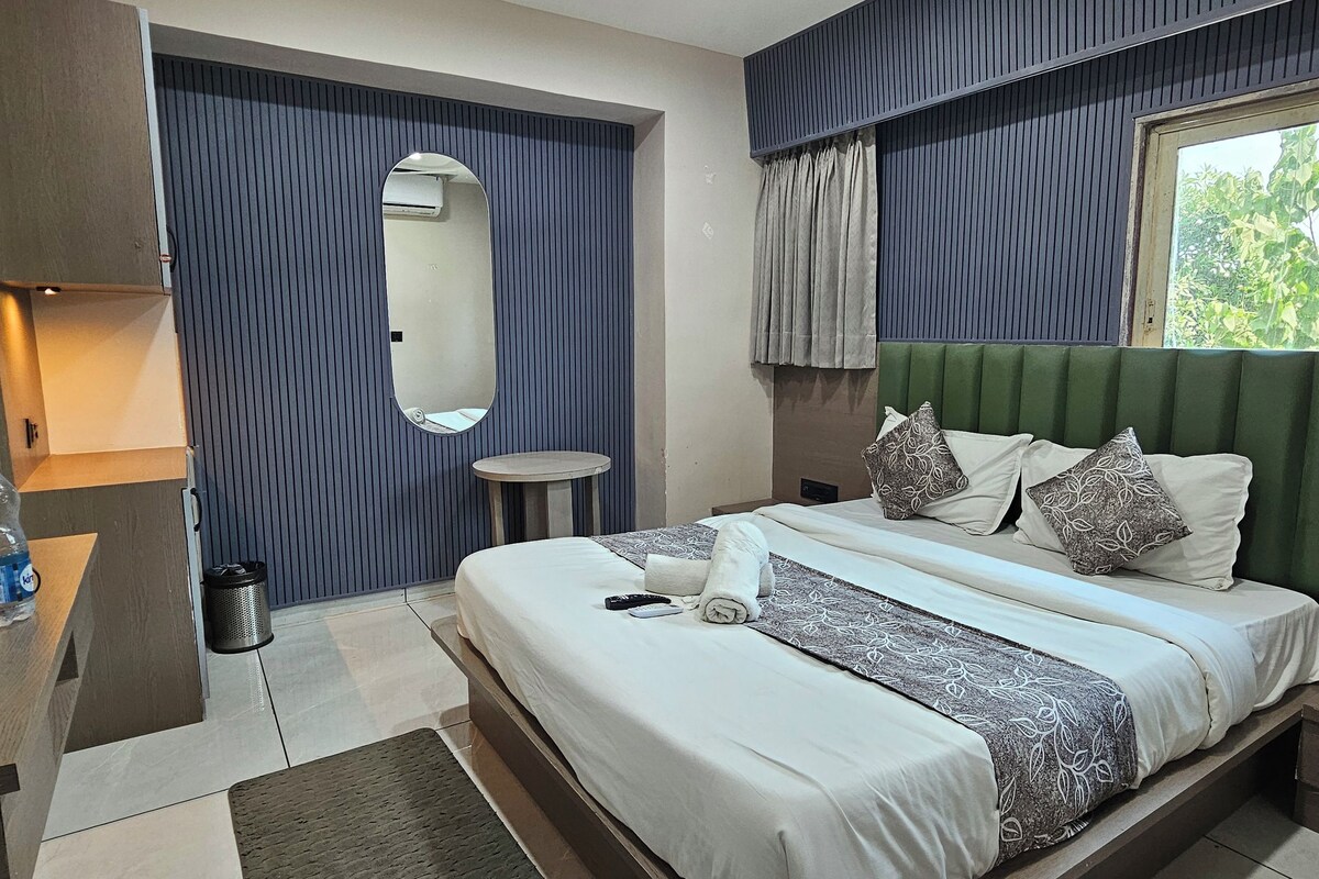 A hotel room with a bed, bedside table, mirror, and a window with curtains.