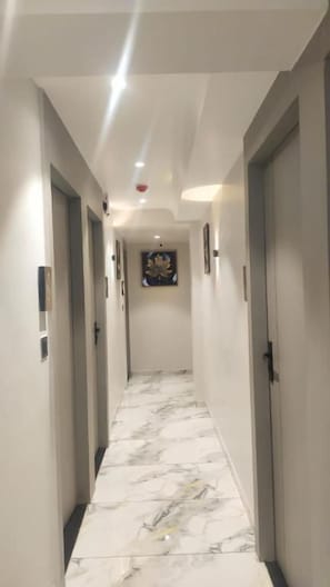 Un pasillo con piso de mármol, puertas a ambos lados y una lámpara en el techo.