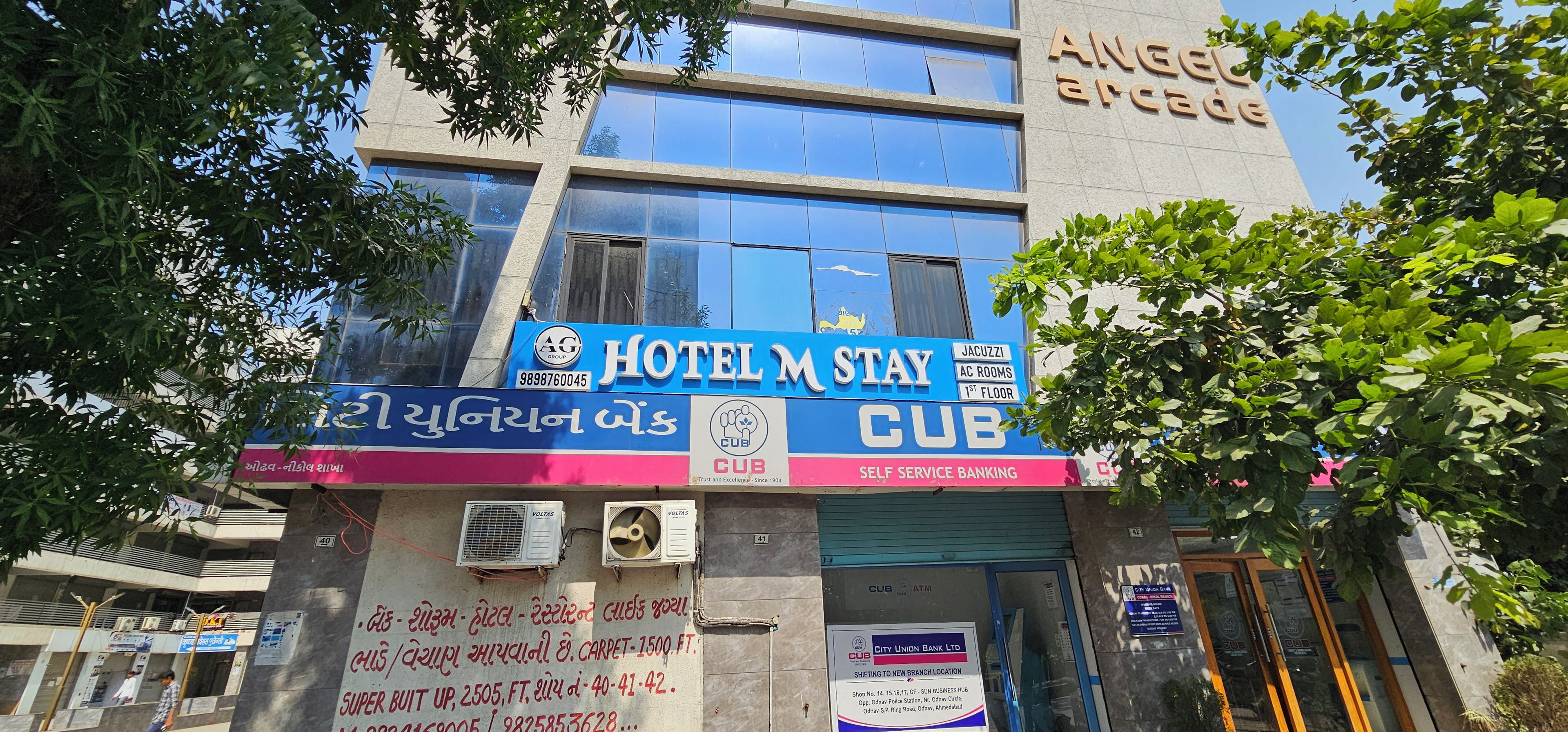 A hotel with a blue signboard, air conditioning units, and a visible ATM.
