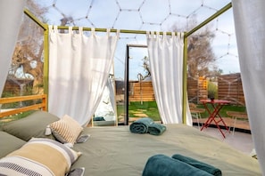 A room with a bed, curtains, a small table, and a view of the outdoors.