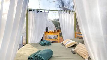Una cama individual con toallas enrolladas, una mesita de noche con artículos de aseo y vistas a través de una ventana con cortinas.