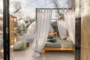 Un dormitorio con cama, mesita de noche, una silla y ventana con vista a árboles.