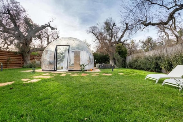A transparent dome structure in a backyard with a lawn, a wooden fence, and two white lounge chairs. - folià (san vito dei normanni)