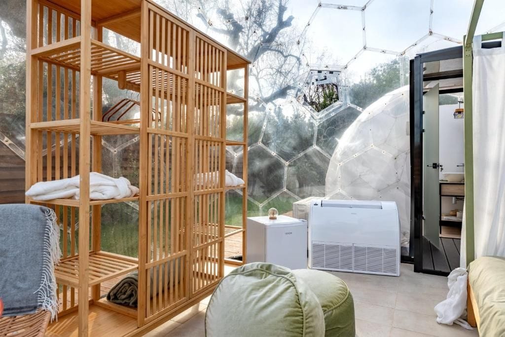 Habitación con una estantería de madera, un equipo de aire acondicionado blanco y vistas a través de una estructura de cúpula de vidrio.