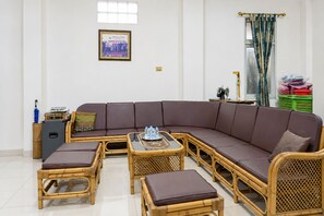 Un salon comprenant un canapé d’angle, deux fauteuils, une table basse et une petite table sur laquelle se trouve un plateau avec des bouteilles.