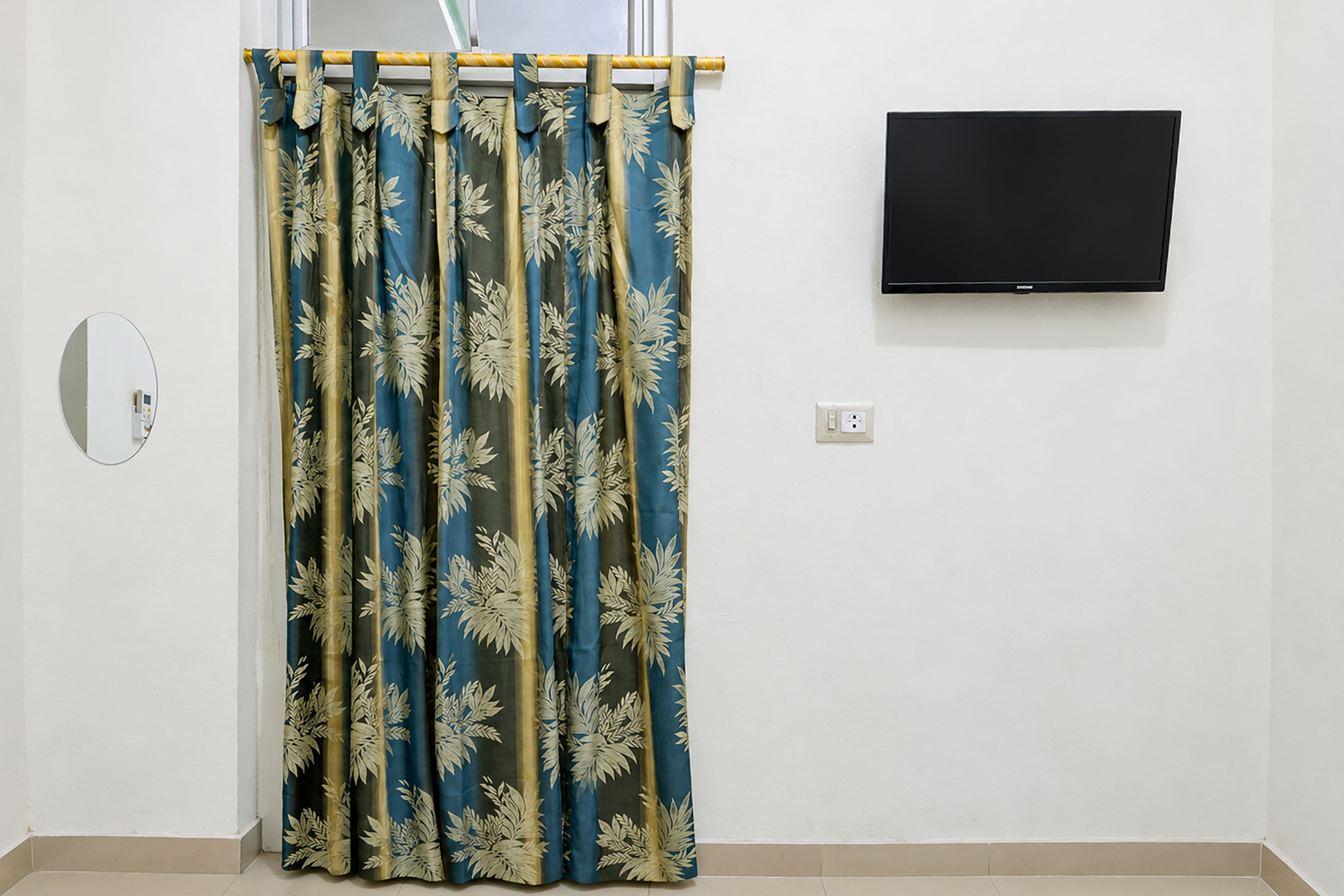 Ein Zimmer mit Vorhang mit Blättermotiv, einem an der Wand montierten Fernseher und einer Steckdose.