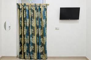 Une pièce avec un rideau orné d’un motif de feuilles, un téléviseur fixé au mur et une prise de courant.