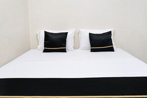 Cama com roupa de cama branca e duas almofadas pretas com detalhes dourados.
