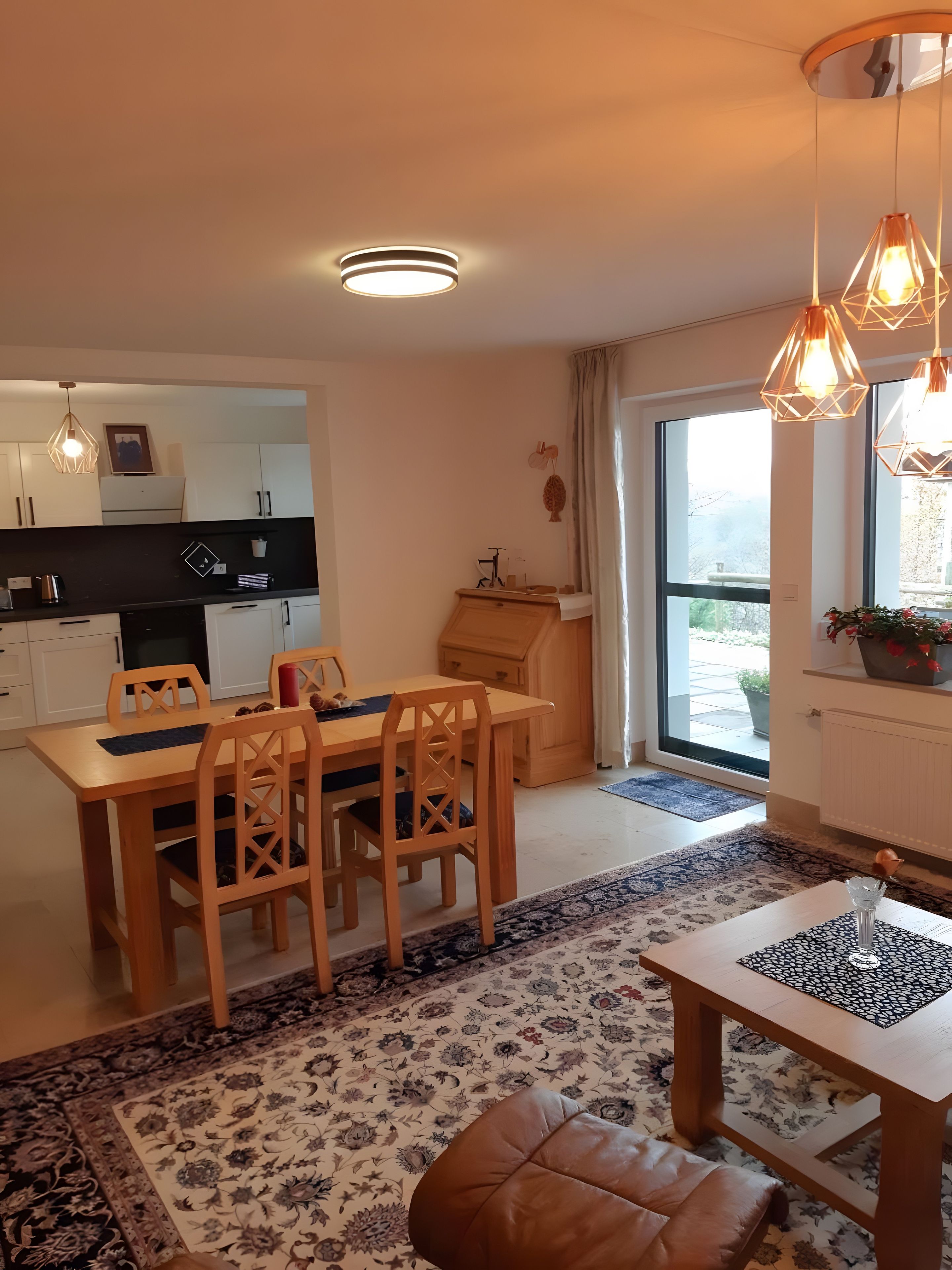 Eine moderne Küche mit weißen Schränken, einem Esstisch mit Stühlen und einem großen Fenster.