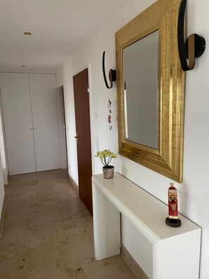 Un couloir avec une console blanche, un miroir à cadre doré et une plante en pot.