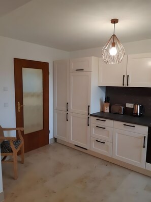 Eine Küche mit weißen Schränken, einem Holzbstuhl, einer Hängelampe und einem Toaster auf der Arbeitsfläche.