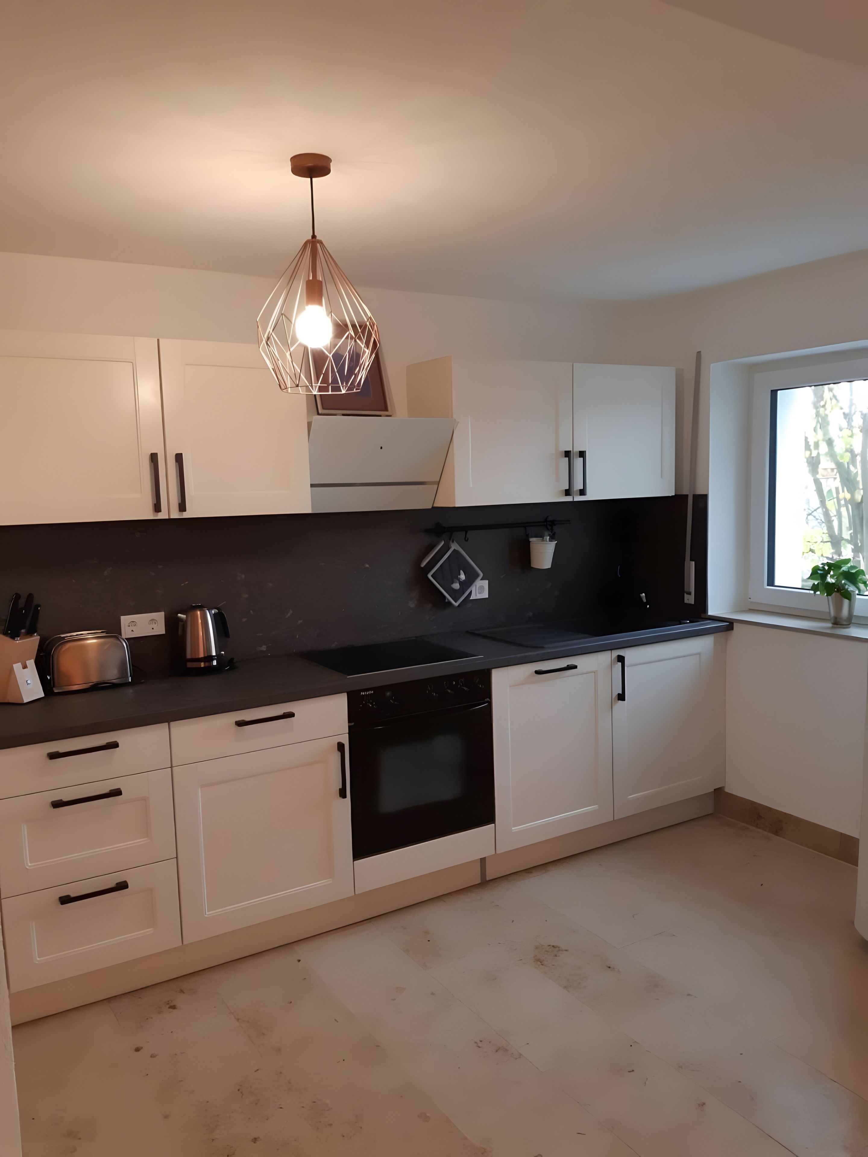 A modern kitchen with white cabinets, a black countertop, and a unique geometric pendant light.