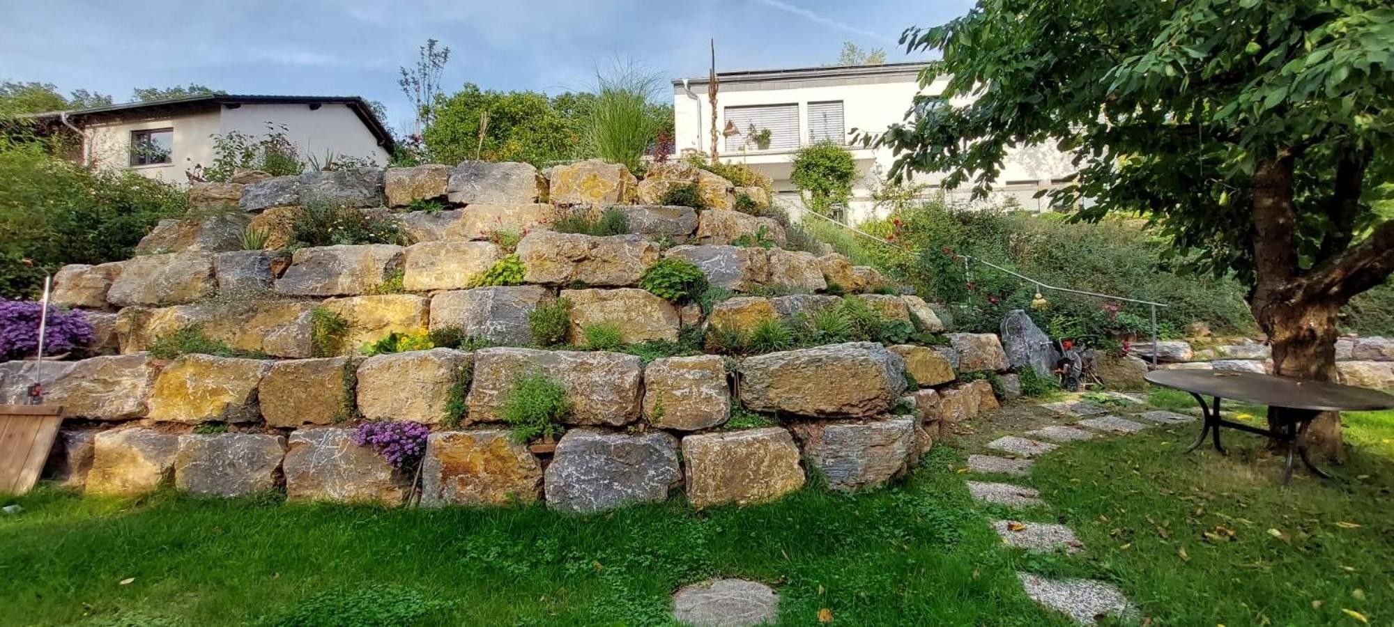 Ein Garten mit einer Steinmauer, einem Baum und einem Tisch.