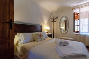 A hotel room with a bed, a nightstand, a lamp, a mirror, and a window with curtains.