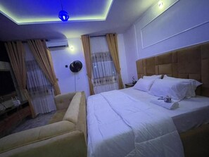 Une chambre d’hôtel avec un lit, un canapé, un ventilateur de plafond et une fenêtre avec des rideaux.