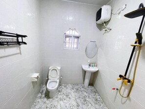 A bathroom with a toilet, sink, shower, and a window.