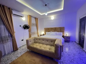 A bedroom with a large bed, a sofa, an air conditioning unit, and a ceiling fan. - MAGS RESIDENCE (Asubi)